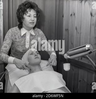 Anni '70, storico, una donna che si trova sulla schiena in un salone con trattamento della pelle, tramite ventose sul collo, Inghilterra, Regno Unito. Cupping è una terapia alternativa che utilizza ventose per stimolare e illuminare la pelle, con una maggiore circolazione sanguigna. Foto Stock
