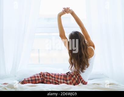 Vista posteriore della donna che si allunga nel letto dopo il risveglio, entrando nuovo giorno felice e rilassante Foto Stock