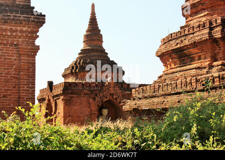 Pagode in mattoni con Buddha color oro all'interno e foglie verdi in primo piano a Bagan, Myanmar Foto Stock