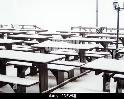 Tavoli identici in legno con panche ricoperte di neve in piedi una fila sulla terrazza di un caffè di strada Foto Stock