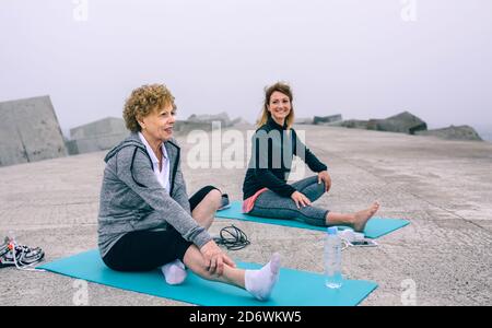 Donna anziana che allunga le gambe con allenatore Foto Stock