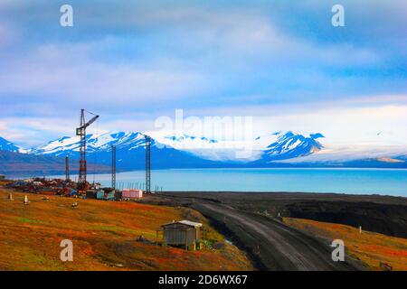 Bella vista panoramica del golfo blu sotto le montagne aride con neve che si scioglie, strada del deserto e gru abbandonate vicino a Barentsburg, Spitsbergen (Svalb Foto Stock