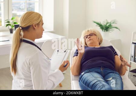 La paziente femminile anziana sdraiata su un lettino medico spiega a una giovane donna dottore la sua salute. Foto Stock