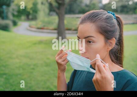 Donna che mette su una maschera chirurgica per la prevenzione del coronavirus. Ragazza asiatica seria usando la copertura di grado medico Foto Stock