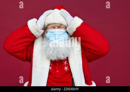 Malato Babbo Natale indossando maschera viso sensazione di mal di testa su sfondo rosso. Foto Stock