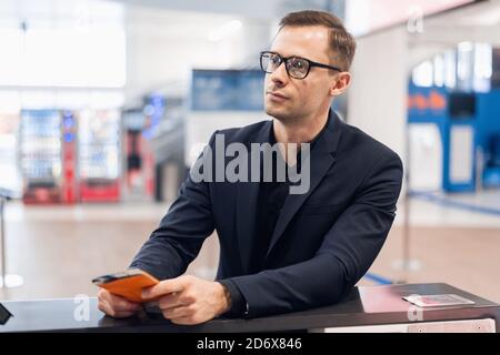 Vista laterale di uomo bello con gli occhiali che dà il passaporto per il personale al banco per il check in all'aeroporto Foto Stock