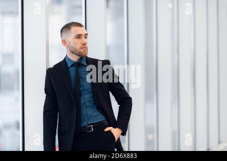 Ritratto di giovane fiducioso elegante uomo d affari con due mani incrociate vicino alla finestra. Foto Stock