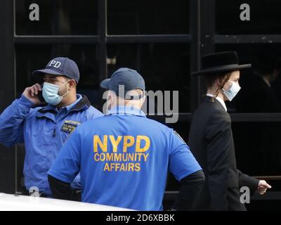 Brooklyn, Stati Uniti. 19 Ott 2020. Gli ufficiali degli Affari comunitari della NYPD si trovano sul marciapiede mentre la gente si riunisce presso la sinagoga Yetev Lev D'Fatmar nel quartiere Williamsburg di Brooklyn a New York City lunedì 19 ottobre 2020. La congregazione di Brooklyn ha pianificato un matrimonio Chassidico che i funzionari statali si aspettavano 10,000 persone a partecipare lunedì ha annunciato che non andrà più come previsto dopo che le autorità hanno ordinato una partecipazione limitata a causa del uptick nelle infezioni da coronavirus. Foto di John Angelillo/UPI Credit: UPI/Alamy Live News Foto Stock