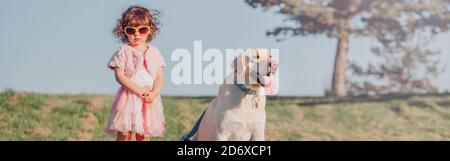 Carino elegante bambina caucasica in occhiali da sole cane da passeggio nel parco campo esterno in estate soleggiato giorno. Capretto che gioca con animale domestico animale domestico. Felice Foto Stock