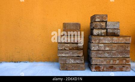 Pila di mattoni di fronte al muro arancione Foto Stock