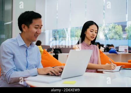 Uomo d'affari e donna asiatici sorridenti e che lavorano insieme, scrivendo in taccuino, collaborazione, collaborazione, lavoro di squadra Foto Stock