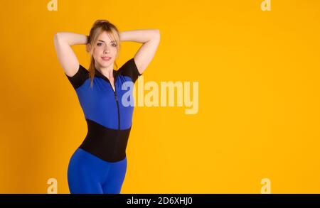 allenatore di fitness ragazza in un jumpsuit blu su un giallo Sfondo un atleta giovane pone e guarda la fotocamera e sorrisi Foto Stock