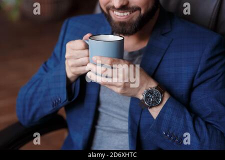 Primo piano mano di un giovane uomo d'affari sorridente in una tazza di caffè Foto Stock