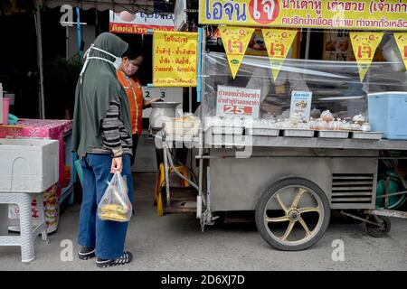 Donna musulmana che acquista nella tradizionale hijab capo copertura per il cibo Ad un carrello di cibo di strada della Thailandia Foto Stock
