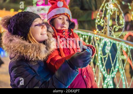 Piccolo ragazzo e sua madre con sparklers vicino all'abeto gigante e illuminazione di Natale sul mercato di Natale. Vacanze di Natale in fiera Foto Stock