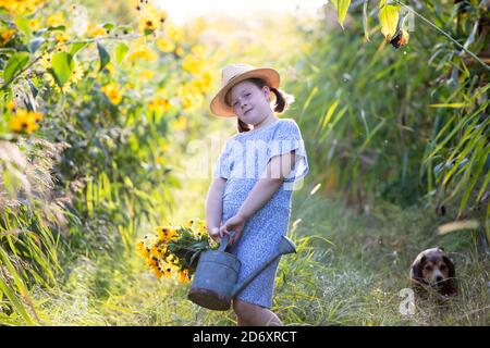 Bambina che cammina su un piccolo sentiero che tiene un annaffiatoio annata può pieno di fiori d'autunno. Foto Stock