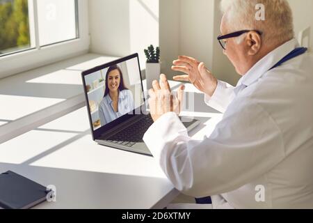 Medico senior seduto alla scrivania in ufficio e dando online consultazione a donna felice Foto Stock