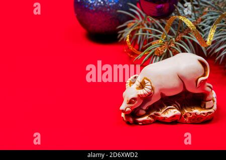 Foto brillante di un toro di Capodanno su sfondo rosso. Un rametto di albero di Natale e una palla con un posto per il testo. Spazio di copia. Foto Stock