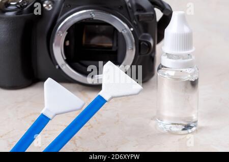 Detergente per sensore di liquido e due tamponi contro la fotocamera dslr con l'obiettivo rimosso. Pulizia di routine di polvere e macchie da apparecchiature fotografiche. Manutenzione Foto Stock