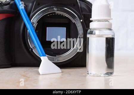 Fotocamera DSLR con specchio rialzato, pulitore per sensore di liquido e bastoncino di cotone su un tavolo. Pulizia di routine di polvere e macchie da apparecchiature fotografiche. Manutenzione Foto Stock