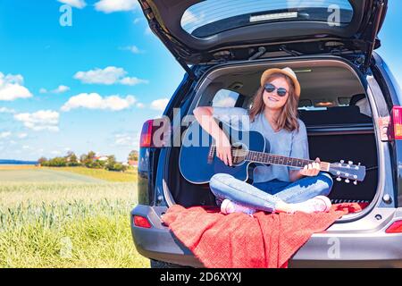 una giovane ragazza che si cimenta con la chitarra in auto sul viaggio in campagna Foto Stock