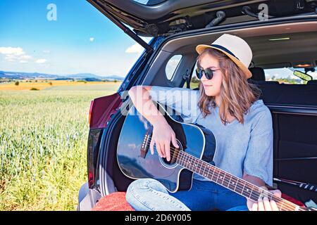 una giovane ragazza che si cimenta con la chitarra in auto sul viaggio in campagna Foto Stock