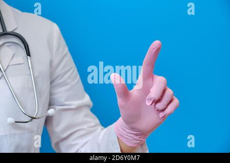 Indossate un guanto medico con un dito che preme un pulsante virtuale, bockup primo piano. Medico in un uniforme medica con una mano su uno sfondo blu, copia s Foto Stock