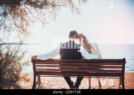 Una sposa e uno sposo seduto panca di legno sulla spiaggia vista posteriore Foto Stock