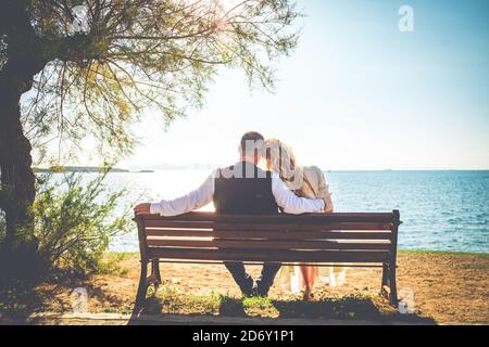 Una sposa e uno sposo seduto panca di legno sulla spiaggia vista posteriore Foto Stock