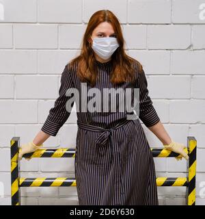 Una barriera protettiva contro una parete bianca e una ragazza con i capelli rossi in una maschera medica. Concetto di lotta dei medici contro le malattie e l'influenza v Foto Stock