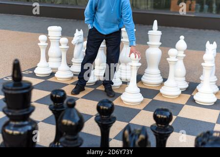 Uomo che gioca a scacchi giganteschi all'aperto. Scacchiera esterna con grandi pezzi di plastica. Scacchi giganti nella zona pubblica. Primo piano grandi pezzi e gigante Foto Stock