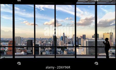 profilo delle donne turistiche scattare foto dello skyline della città da un osservatorio. tramonto nel moderno quartiere degli affari urbani. acciaio cornice rosa wi Foto Stock