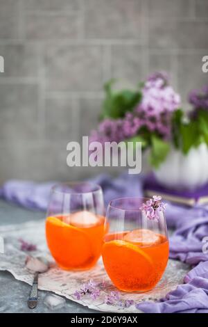 Cocktail Orange Aperol Spritz servito in un bicchiere di vino, decorato con una fetta di arancia e lilla Foto Stock