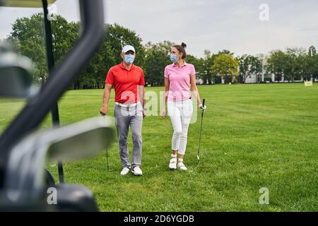 Due golfisti in maschere protettive che attraversano il campo da golf Foto Stock
