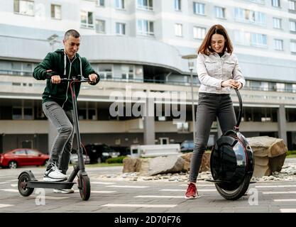 Giovane uomo che guida elettrica kick scooter e giovane donna dentro uniciclo informale sulla strada della città Foto Stock