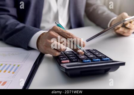 uomo d'affari che analizza grafici finanziari e grafici in ufficio con calcolatrice e tablet digitale. rapporti aziendali, analisi dei dati Foto Stock