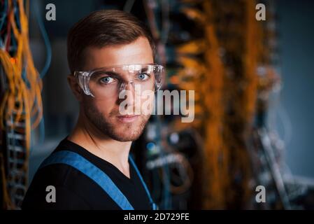 Giovane uomo in uniforme lavora con attrezzature internet e fili nella sala server Foto Stock