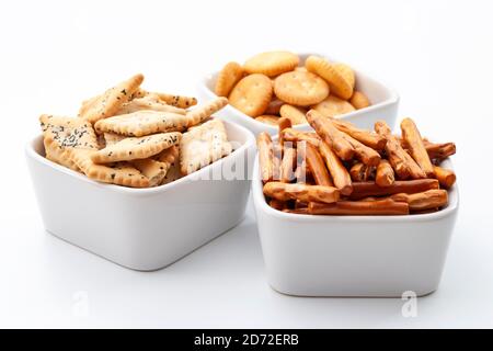 Selezione di pretzel misti, bastoncini, cracker e spuntini salati in ciotole bianche in ceramica isolate su sfondo bianco Foto Stock