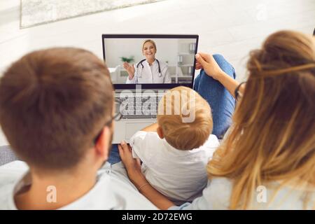 Una giovane famiglia con un figlio effettua una videochiamata via computer portatile a un pediatra per consigli e consigli. Foto Stock