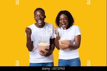 Eccitato uomo nero e donna mangiare popcorn su sfondo giallo Foto Stock