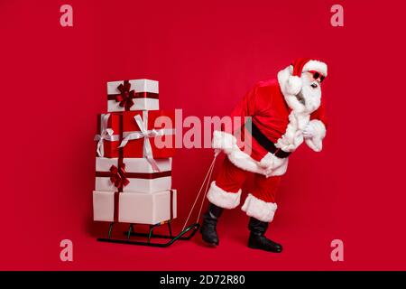 Attacco di cuore. Foto a lunghezza intera del vecchio uomo ritirato barba bianca tenere pesante slitta giftbox passeggiata consegnare l'abbigliamento attuale santa x-mas costume cappotto da sole Foto Stock