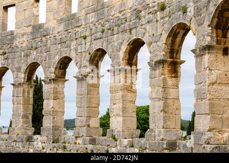 Dettagli di archi e colonne nelle pareti esterne dell'iconico antico anfiteatro romano di Pola, Istria, Croazia, una delle principali attrazioni turistiche Foto Stock