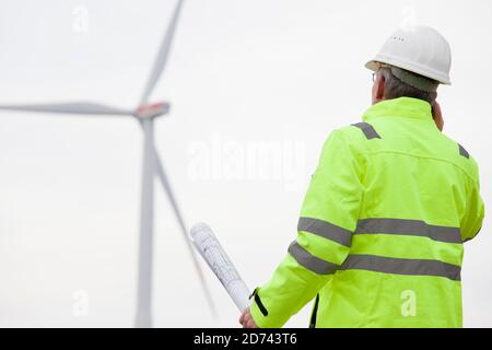 Ingegnere maturo che parla sul telefono cellulare di fronte a un turbine eoliche con il modello in mano - fuoco sopra la persona Foto Stock