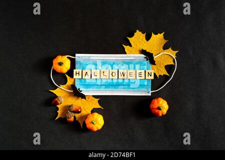 Zucche di Halloween, maschera medica protettiva e foglie di acero giallo su sfondo nero, pipistrelli di carta nera. L'iscrizione HALLOWEEN il Foto Stock