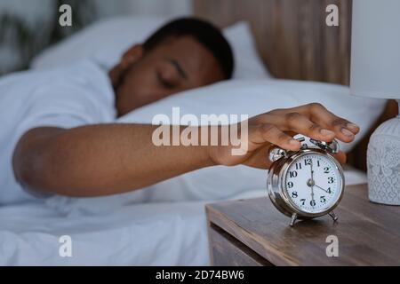 Risveglio dell'uomo africano spegnimento dell'orologio di allarme sdraiato nel letto Foto Stock