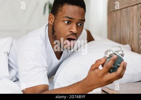 Scioccato Black Guy guardando sveglia svegliarsi oversleeping in interni Foto Stock