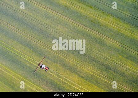 Punto di vista del drone di un trattore che spruzza su un campo coltivato. Foto Stock