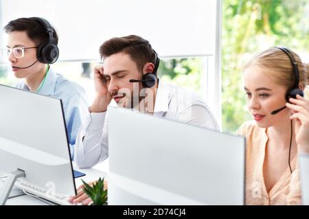 Un rappresentante del call center stanco e i suoi colleghi al lavoro ufficio open space Foto Stock