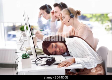 Consulente hotline stanco che dormiva alla sua scrivania, sentendosi sfinito o stressato dopo la comunicazione con i clienti Foto Stock