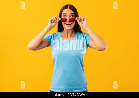 Entusiasta donna sorpresa che guarda la macchina fotografica togliere gli occhiali da sole Foto Stock
